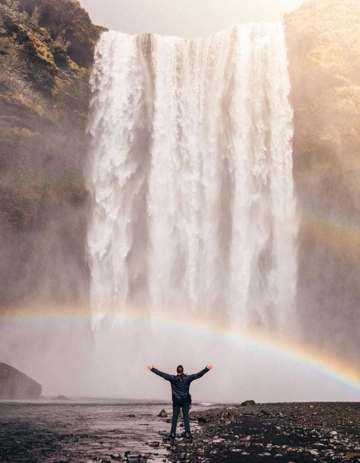 Figure with arms raised in front of a waterfall