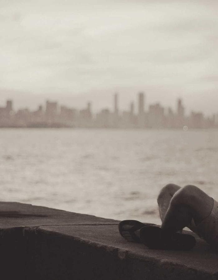 Figure seated by the water at sunset with a city skyline